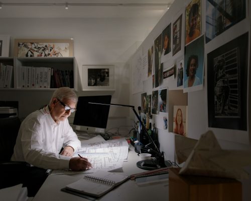 Wide angle photo of Richard Henriquez, founding principal of Henriquez Partners Architects at work at his desk in Vancouver, BC.