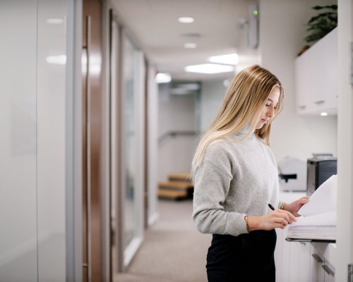 Young caucasian female writing in open binder in hallway of law firm