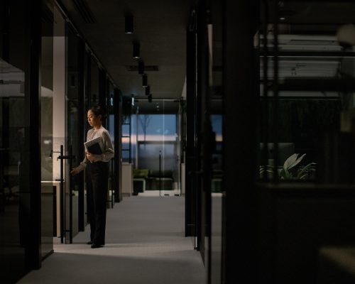 Young asian woman opens glass door in modern office