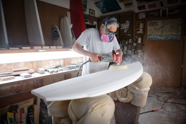 Asian man crafts a surfboard in his workshop