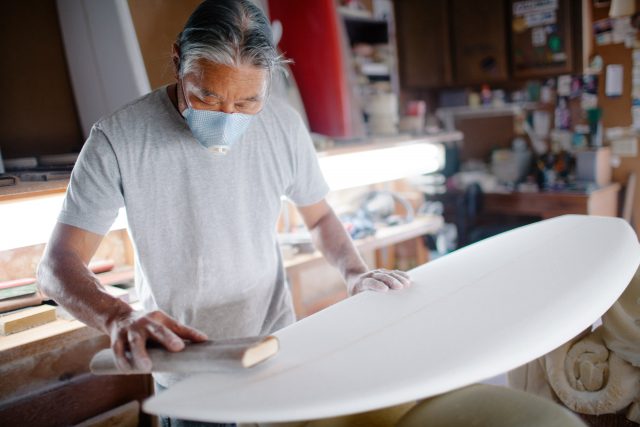 Asian man crafts a surfboard in his workshop